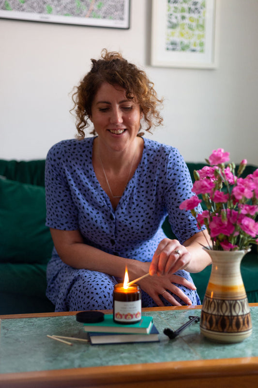 Emma lighting a candle on her coffee table, vase of flowers next to candle.