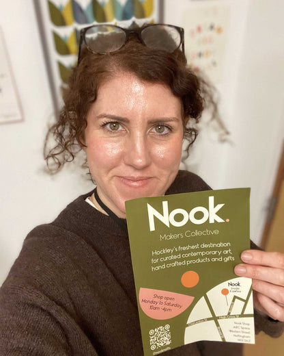Emma from every nook holding a green 'Nook' flyer with a map on a white wall background